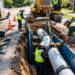 Workers installing a new PVC pipe in a trench during a residential sewer pipe replacement project
